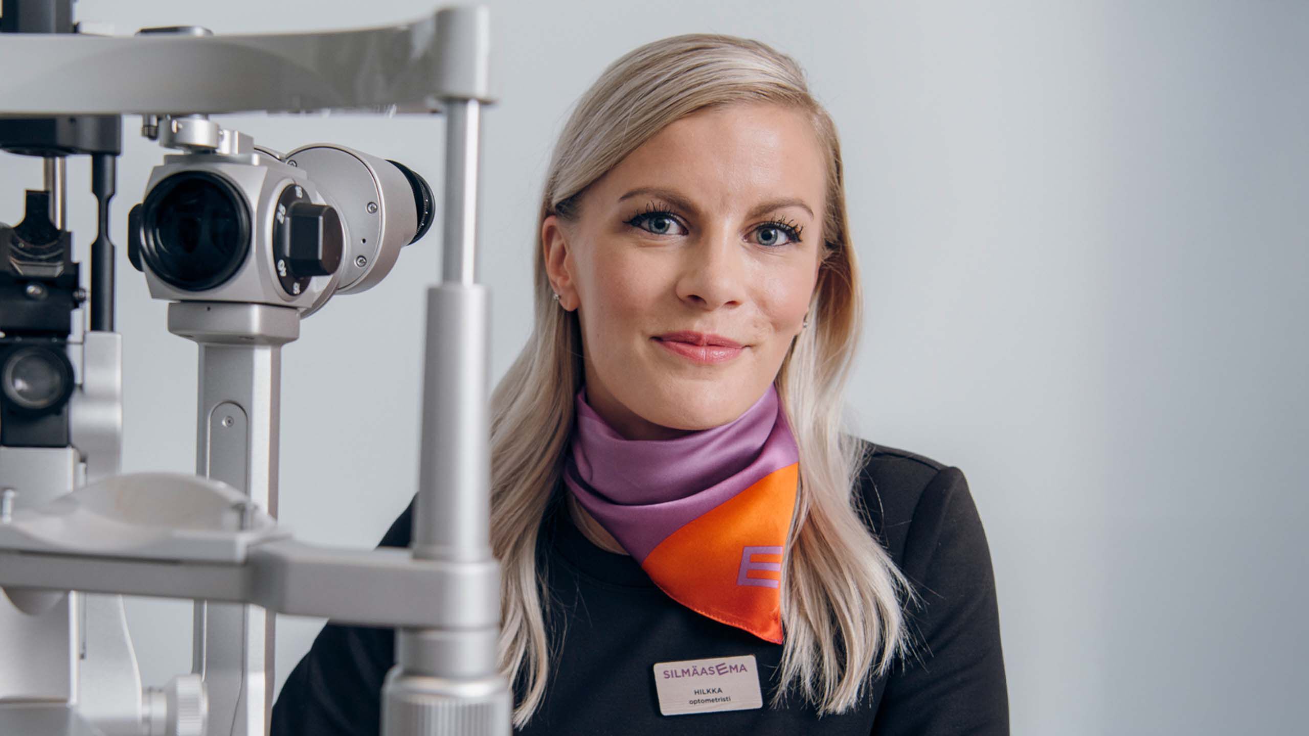Optikko hymyilee kameralle mikroskoopin edess&auml;.